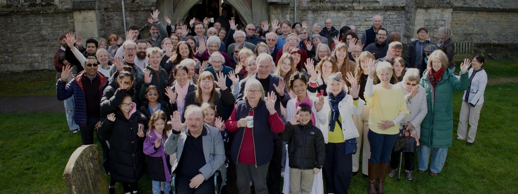 A group of church members, waving and smiling, standing in front of St Mary's church.