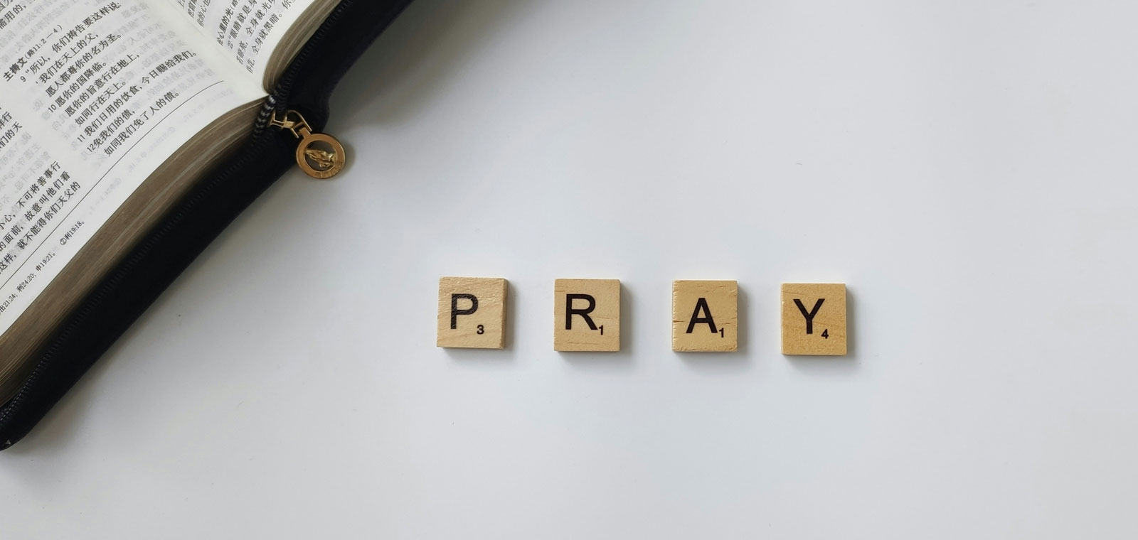 An open Bible with the word "PRAY" spelt out in letter tiles.