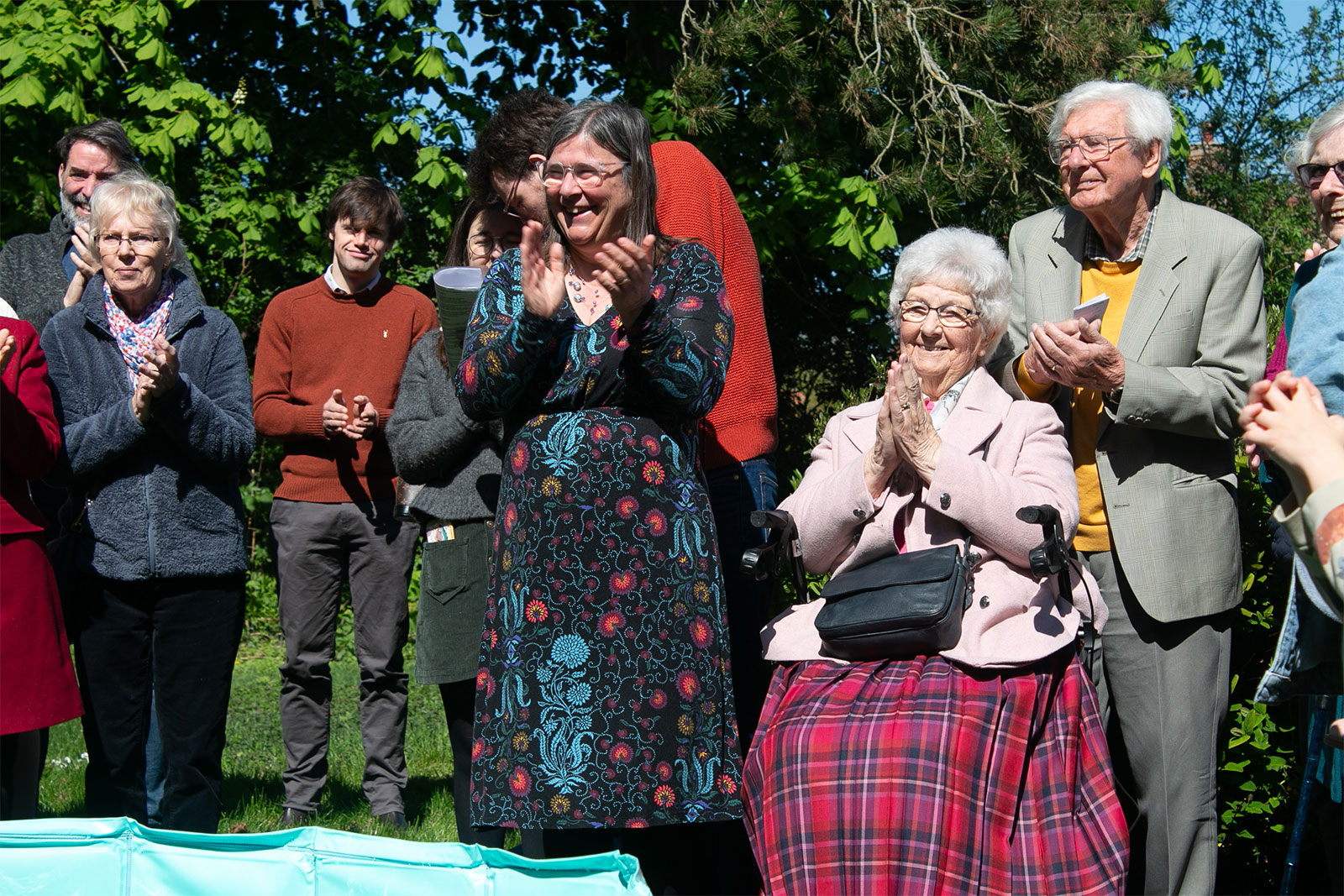 A group of people outdoors, smiling and clapping.